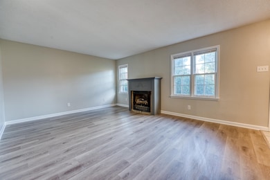 Unfurnished living room with wood finished floors, a fireplace with flush hearth, and baseboards