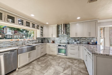 Kitchen with appliances with stainless steel finishes, light stone counters, wall chimney exhaust hood, backsplash, and a peninsula