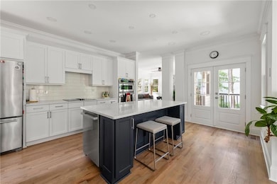 Kitchen with appliances with stainless steel finishes, a breakfast bar area, white cabinetry, decorative backsplash, and a center island