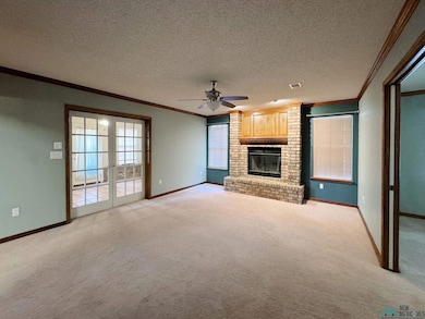 Unfurnished living room featuring a textured ceiling, ornamental molding, a fireplace, french doors, and light colored carpet