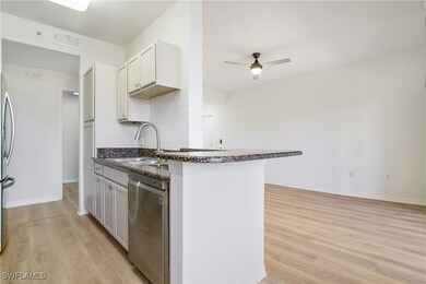 Kitchen featuring appliances with stainless steel finishes, a sink, light wood-style flooring, ceiling fan, and dark stone countertops