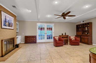 Living room featuring ceiling fan, a brick fireplace, built in shelving, light tile flooring, and french doors