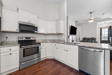 Kitchen featuring stainless steel appliances, white cabinetry, a peninsula, dark wood finished floors, and light stone countertops