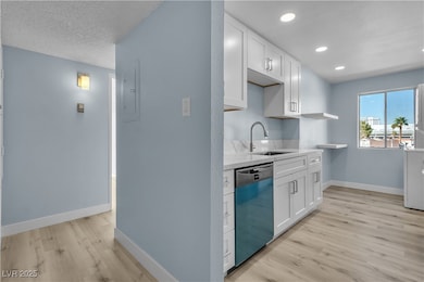 Kitchen featuring light wood-style flooring, dishwasher, white cabinets, light countertops, and open shelves