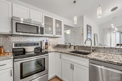Kitchen featuring stainless steel appliances, white cabinets, glass insert cabinets, tasteful backsplash, and vaulted ceiling
