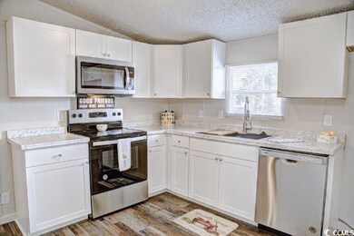 Kitchen featuring stainless steel appliances, a sink, light wood-style flooring, white cabinetry, and a textured ceiling