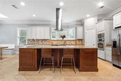 Kitchen featuring an island with sink, stainless steel appliances, island range hood, white cabinets, and backsplash