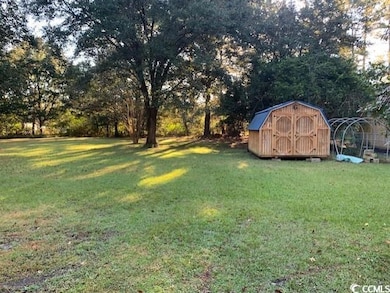 View of green lawn with a storage shed and view of wooded area