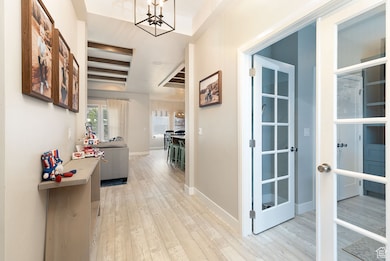Corridor featuring light wood-style flooring, a chandelier, and a raised ceiling
