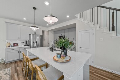 Kitchen with stainless steel fridge, dark hardwood / wood-style flooring, tasteful backsplash, sink, and a center island with sink