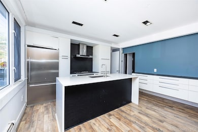 Kitchen featuring modern cabinets, white cabinetry, freestanding refrigerator, and light wood-style floors