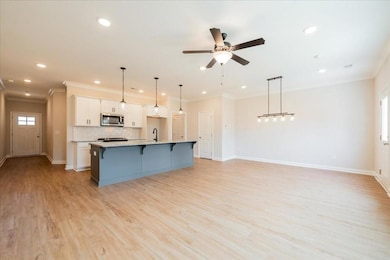 MODEL REPRESENTATIVE- Kitchen with ornamental molding, white cabinetry, pendant lighting, open floor plan, and a kitchen bar