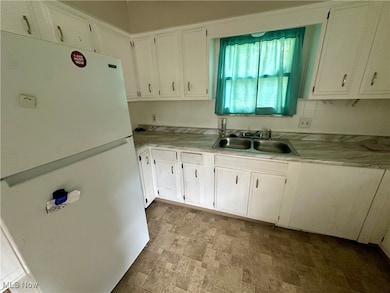 Kitchen with freestanding refrigerator, light countertops, stone finish flooring, and white cabinetry