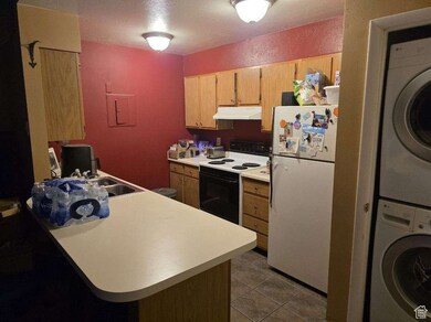 Kitchen featuring range with electric stovetop, freestanding refrigerator, light countertops, stacked washer / drying machine, and under cabinet range hood