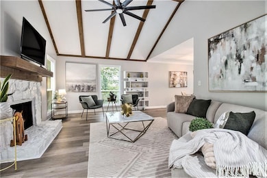Living area featuring ceiling fan, high vaulted ceiling, beamed ceiling, baseboards, and a fireplace