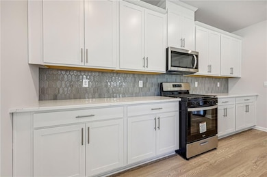 Kitchen featuring appliances with stainless steel finishes, light wood-style floors, white cabinetry, decorative backsplash, and light stone countertops