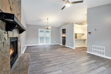Unfurnished living room featuring a chandelier, a fireplace, ceiling fan, high vaulted ceiling, and wood finished floors