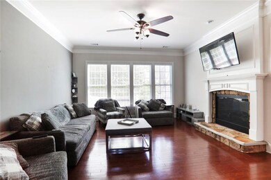 Living area with a glass covered fireplace, ceiling fan, ornamental molding, dark wood-type flooring, and visible vents