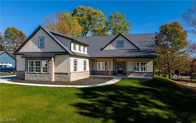 View of front facade with a front lawn, covered porch, stone siding, and roof with shingles