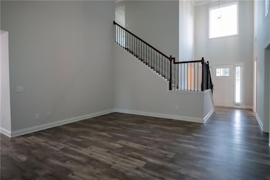 Unfurnished living room featuring a towering ceiling, dark wood-type flooring, and stairway