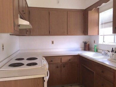 Kitchen space with electric stove, wood cabinetry 