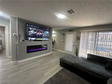 Living room with a textured ceiling, wood finished floors, and a glass covered fireplace