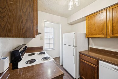 Kitchen with dark countertops, white appliances, a textured ceiling, dark wood-style floors, and brown cabinets