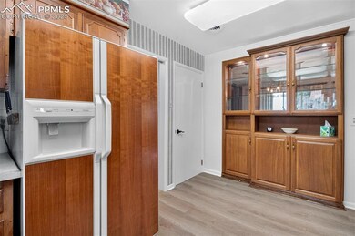 Kitchen featuring white refrigerator with ice dispenser, brown cabinetry, light wood finished floors, and light countertops