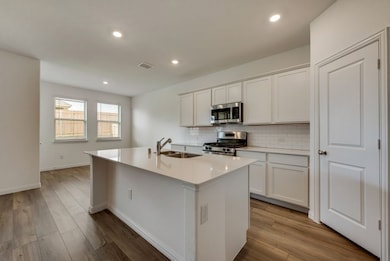 Kitchen featuring tasteful backsplash, appliances with stainless steel finishes, an island with sink, light countertops, and recessed lighting