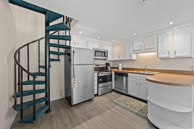 Kitchen featuring stainless steel appliances, white cabinetry, a textured ceiling, wood finished floors, and recessed lighting