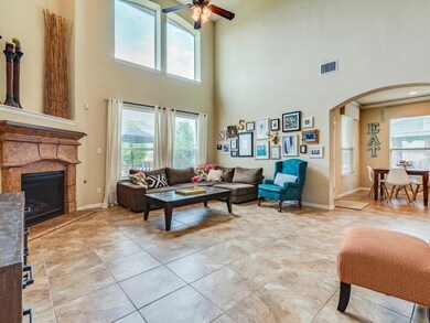 Living room featuring a towering ceiling, ceiling fan, a stone fireplace, arched walkways, and light tile patterned floors