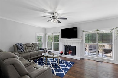 Living area featuring wood finished floors, crown molding, a brick fireplace, and a ceiling fan
