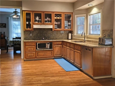 Kitchen featuring brown cabinetry, light stone counters, backsplash, and glass insert cabinets