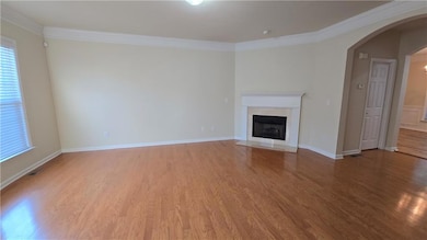 Unfurnished living room with crown molding, arched walkways, light wood-style flooring, a fireplace with flush hearth, and baseboards