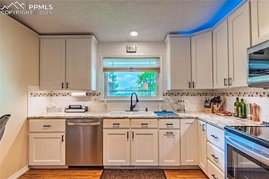 Kitchen featuring stainless steel appliances, wood floors, tasteful backsplash, Touch faucet, and light stone countertops, under and over counter lighting.