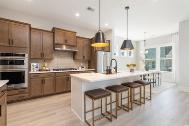 Kitchen featuring backsplash, a breakfast bar, a large kitchen island with sink, cabinets, and decorative light fixtures