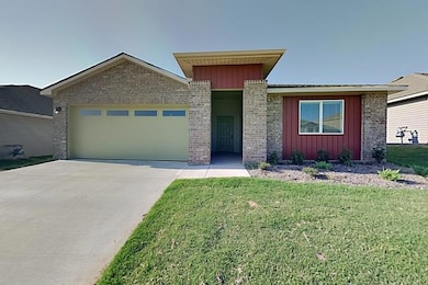 View of front facade featuring board and batten siding, a garage, a front yard, concrete driveway, and brick siding
