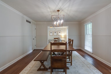 Dining room with wood finished floors, a chandelier, wainscoting, and ornamental molding