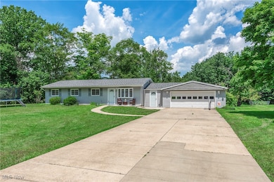 Ranch-style house featuring a trampoline, an attached garage, a front yard, and concrete driveway