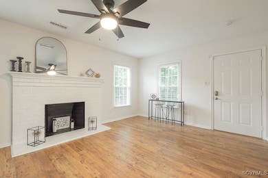Unfurnished living room featuring a ceiling fan, wood finished floors, and a brick fireplace