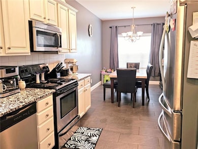 Kitchen with stainless steel appliances, white cabinets, a chandelier, decorative backsplash, and light stone counters