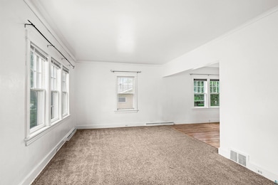 Carpeted spare room featuring crown molding and baseboard heating