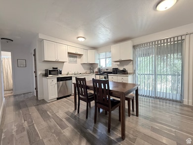 Kitchen featuring white cabinets, light countertops, stainless steel appliances, light wood finished floors, and a textured ceiling