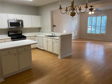 Kitchen with appliances with stainless steel finishes, open floor plan, light countertops, light wood finished floors, and a peninsula