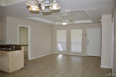 Kitchen with light tile patterned flooring, ceiling fan with notable chandelier, a sink, and a raised ceiling
