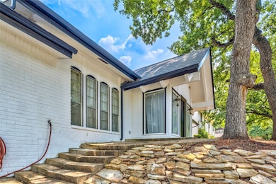 Property entrance featuring brick siding, a patio area, and roof with shingles