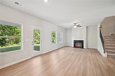 Unfurnished living room with stairs, light wood-style floors, a fireplace with flush hearth, and ceiling fan