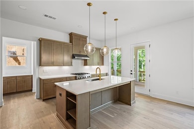 Kitchen with a sink, under cabinet range hood, open shelves, light wood-style flooring, and backsplash
