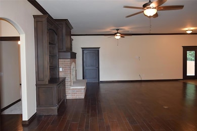 Unfurnished living room with a ceiling fan, arched walkways, baseboards, crown molding, and dark wood finished floors