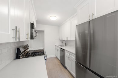 Kitchen featuring appliances with stainless steel finishes, white cabinetry, decorative backsplash, and light stone countertops
